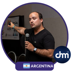 "Daniel Crespo, conferencista argentino, sosteniendo un micrófono mientras da una charla interactiva, con un gesto enfático y un fondo de evento corporativo."