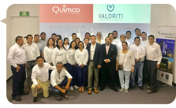 Franco Borges junto a un grupo de colaboradores corporativos en un taller de capacitación empresarial, con los logotipos de Quimco y Valoriti en el fondo.