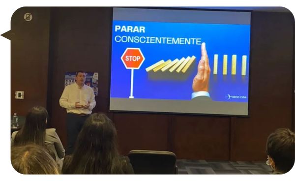 José Illescas durante una conferencia sobre la importancia de detenerse conscientemente, ilustrado con una imagen de fichas de dominó y una señal de alto.