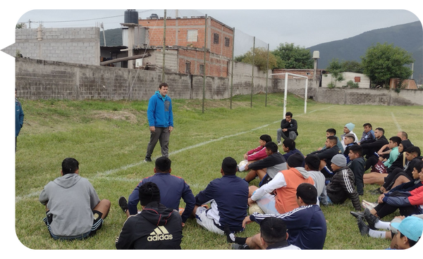 José Illescas hablando a un grupo de jóvenes en un campo de fútbol, compartiendo un mensaje de motivación y liderazgo.