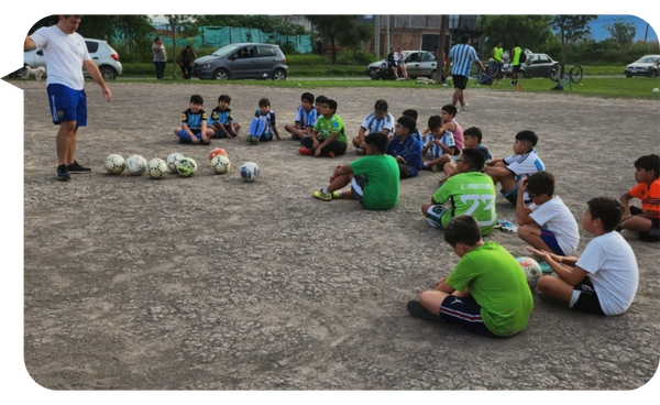 Entrenador motivando a un grupo de niños sentados en un campo de fútbol durante una charla de equipo.