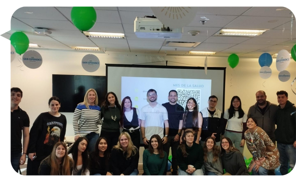 Lorna Burgos junto a un grupo de personas durante una actividad del Mes de la Salud en una sala de conferencias decorada con globos verdes.