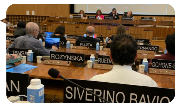 Asistentes y panelistas en una sesión del Comité Internacional de Bioética de la UNESCO, con carteles de nombres visibles y una pantalla de presentación al fondo.