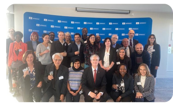 Grupo de expertos y representantes del Comité Internacional de Bioética de la UNESCO posando juntos frente a un fondo con el logotipo de la UNESCO.