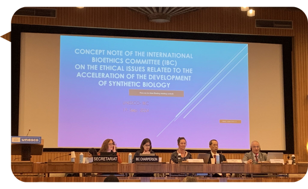 Mesa de discusión en la UNESCO sobre los temas éticos relacionados con el desarrollo de la biología sintética, con panelistas y pantalla de presentación.