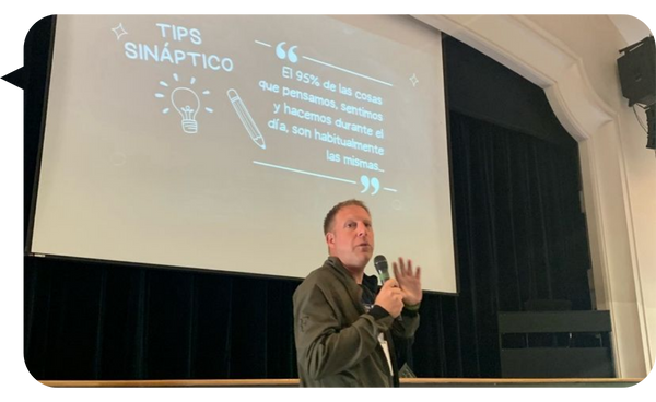 : Rodrigo Cauas Esturillo dando una conferencia, con una diapositiva sobre "Tips Sináptico" proyectada en pantalla.