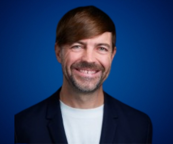 Retrato de Steven MacGregor, conferencista internacional en bienestar corporativo y liderazgo, con fondo azul y sonrisa cálida.