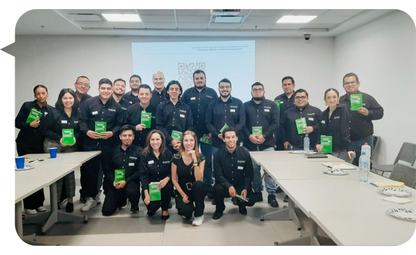 "Yami Almaguer Gil posando con un grupo de participantes en una sala de capacitación, todos sosteniendo libros verdes."