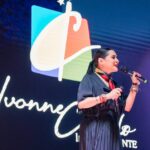 Ivonne Casado, conferencista internacional, impartiendo una charla en escenario con su logotipo de fondo durante un evento de liderazgo transformador.