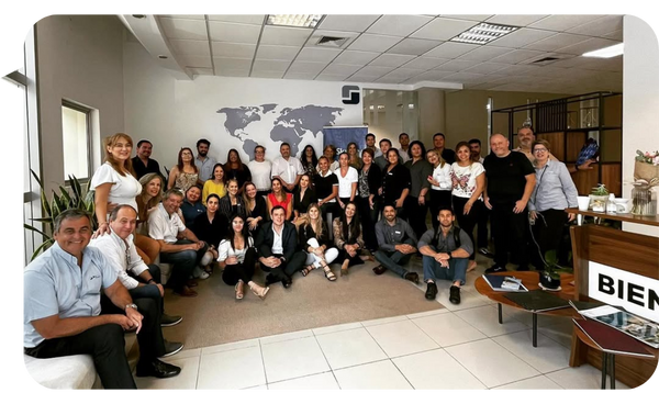 "Daniel Ortiz posando junto a un grupo de profesionales en una oficina moderna con un mapa del mundo en la pared y un ambiente de colaboración."