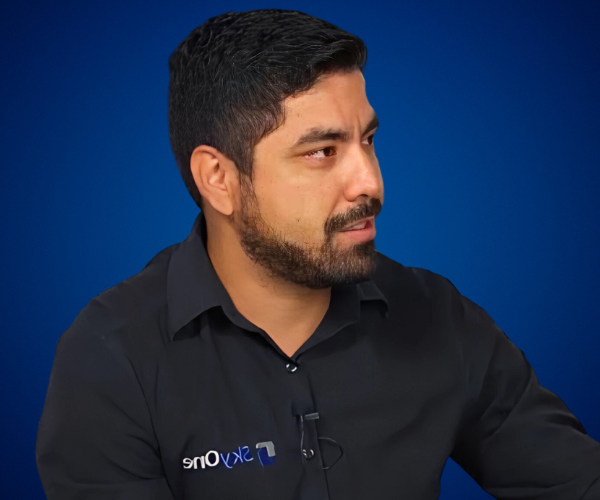 "Daniel Ortiz, CEO de SkyOne Real Estate, vistiendo una camisa negra con el logo de SkyOne, sobre un fondo azul."