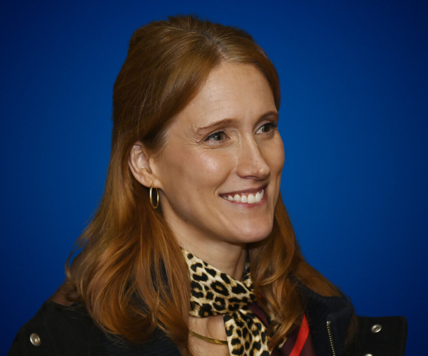 Retrato de Kim Brierley, conferencista internacional especializada en neurociencia aplicada, vistiendo una bufanda de estampado animal y luciendo una sonrisa cálida frente a un fondo azul.