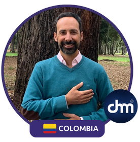 Luis Felipe Avella Villegas en un entorno natural, vistiendo un suéter azul y camisa rosada, con la mano en el pecho, dentro de un marco circular con el logotipo de "dhm" y la bandera de Colombia.