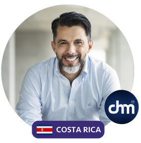 Fotografía de Allan Loria, un profesional sonriente con cabello oscuro y barba, vistiendo camisa blanca, con el logotipo de CHM y la bandera de Costa Rica en la esquina inferior derecha.