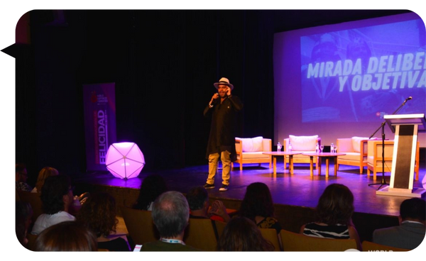 Gaspar Contreras en el escenario durante una conferencia sobre bienestar y felicidad organizacional, dirigiéndose al público con un micrófono en la mano.