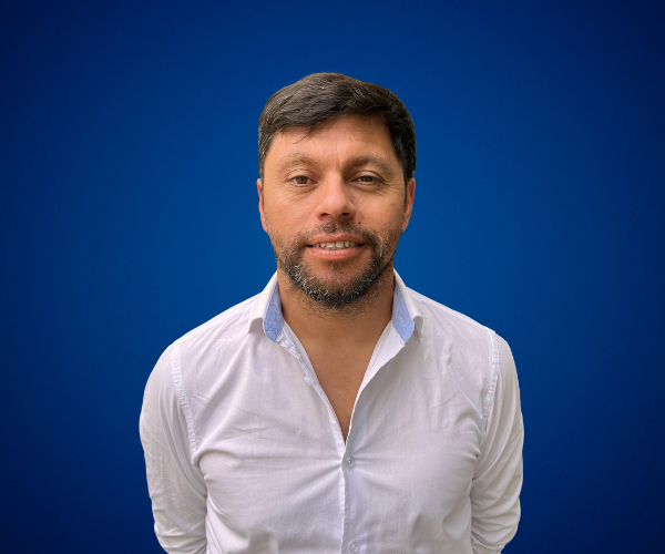 José Miguel González Riffo, conferencista experto en liderazgo personal y felicidad organizacional, posando con una camisa blanca frente a un fondo azul.