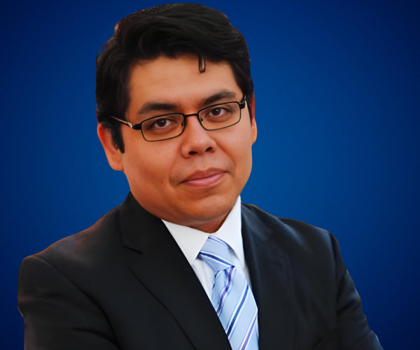 Retrato de Norman Valdez, experto en inteligencia artificial y tecnología ética, vistiendo traje oscuro y corbata azul, con un fondo azul profesional.