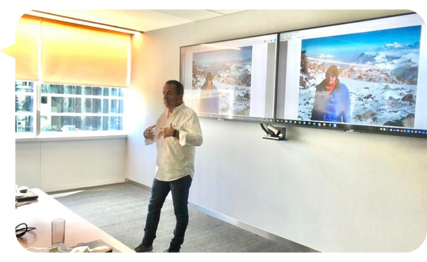 Peter Czanyo impartiendo una conferencia en un ambiente corporativo, con imágenes de sus expediciones en la pantalla.