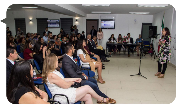 Ariadna Tamayo brindando una conferencia en un evento profesional, con una audiencia atenta en un auditorio moderno.