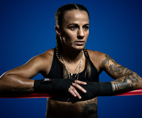 Esther María Micheo Santizo, atleta y conferencista, en pose de boxeo con mirada determinada, vestimenta deportiva y vendajes en sus manos, sobre un fondo azul.