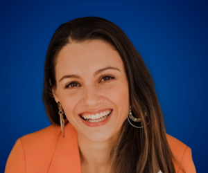 Katterín Rodríguez, conferencista y coach en marca personal, sonriendo con confianza en un fondo azul.