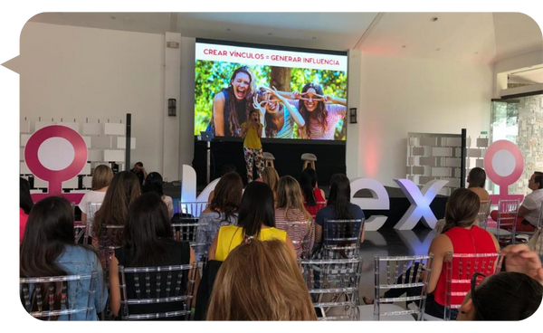 ebeca Barzuna en un evento de empoderamiento femenino, presentando ante una audiencia mayoritariamente femenina en un escenario con una pantalla que muestra el mensaje "Crear vínculos = Generar influencia".