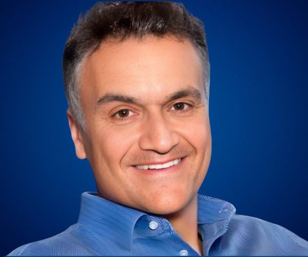 Retrato de Carl Honoré con camisa azul y fondo azul, sonriendo con una expresión amigable y profesional.