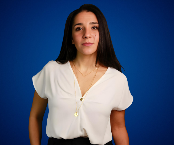 Giovanna Massad posando con confianza sobre un fondo azul, vistiendo una blusa blanca y un collar dorado.