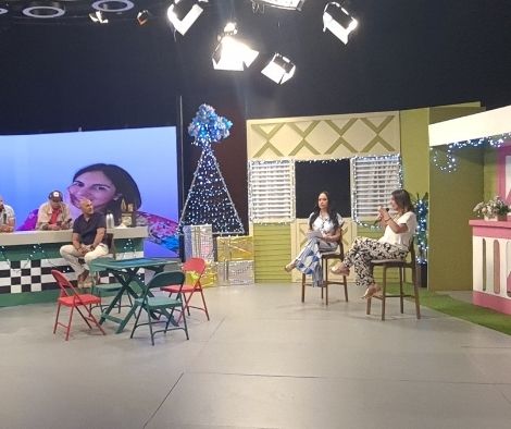 Vivianne Verschae participando en un programa de televisión, sentada junto a otra invitada en un set decorado con temática navideña.