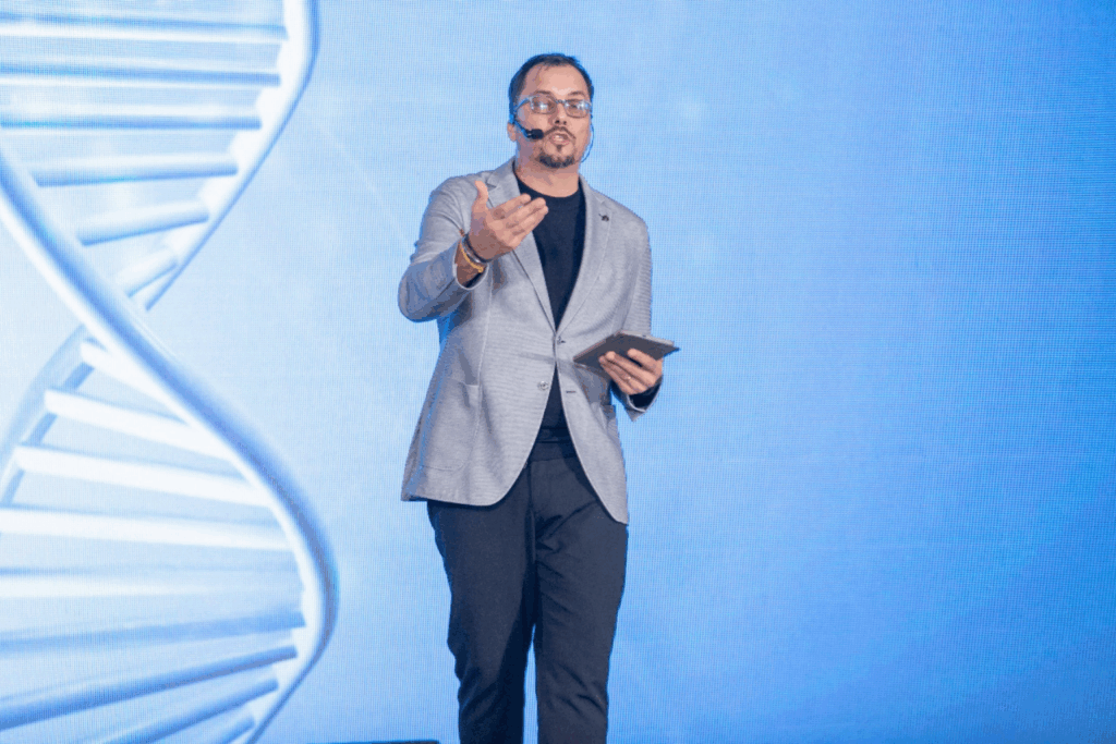 Andrés Conde en escenario durante una conferencia sobre inteligencia artificial y transformación digital, hablando al público con una tablet en la mano.