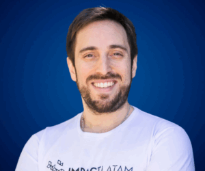 Daniel Tricarico sonriendo con camiseta blanca frente a fondo azul, experto en emprendimiento e innovación.