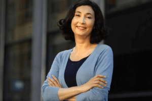 Elsa Punset, experta en inteligencia emocional, sonriente con los brazos cruzados frente a un edificio moderno.