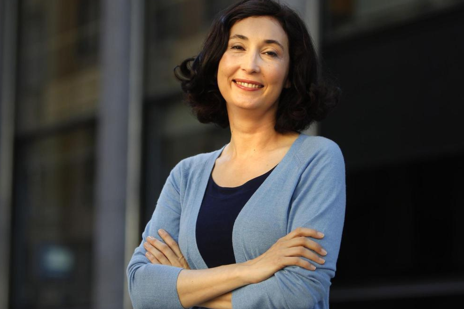 Elsa Punset, experta en inteligencia emocional, sonriente con los brazos cruzados frente a un edificio moderno.