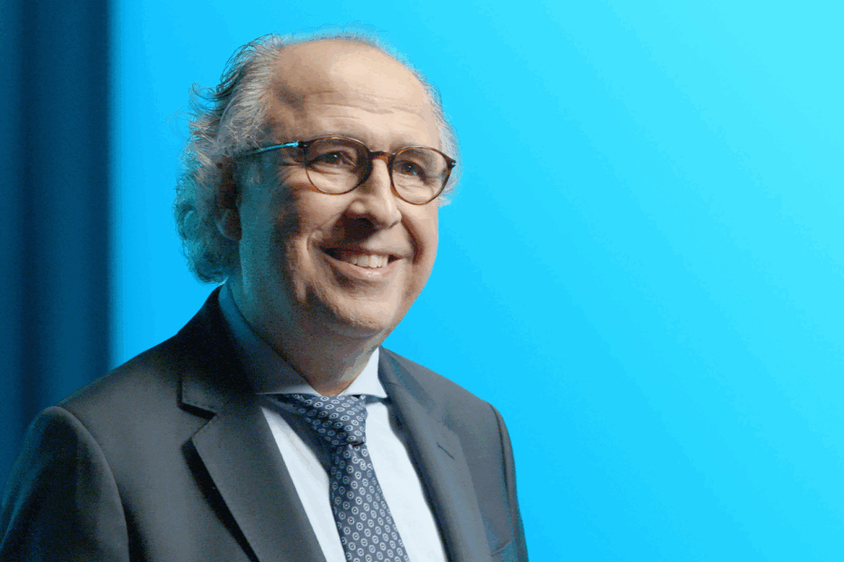 Emilio Duró sonriendo, con traje y corbata, frente a fondo celeste vibrante, transmitiendo energía positiva y entusiasmo.