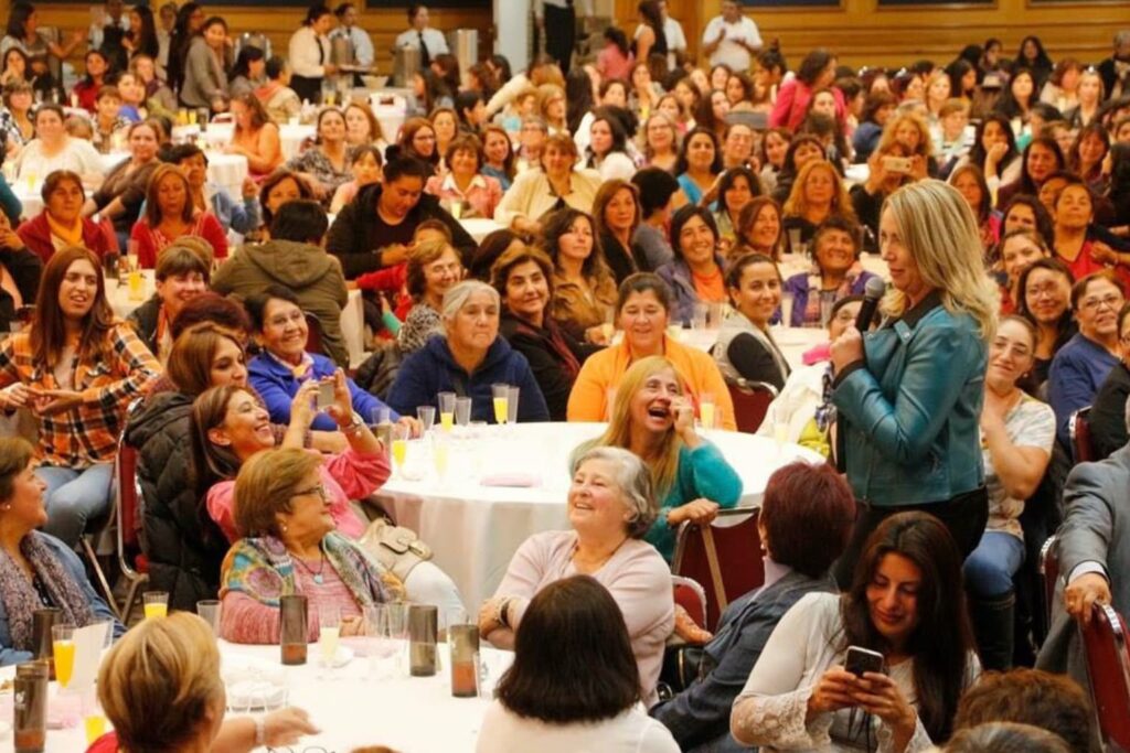 Jennifer Warner dando una conferencia motivacional a un público femenino numeroso y participativo