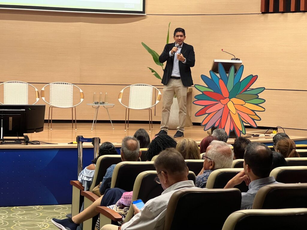 Marcos Burgos dando una conferencia motivacional frente a público en auditorio.