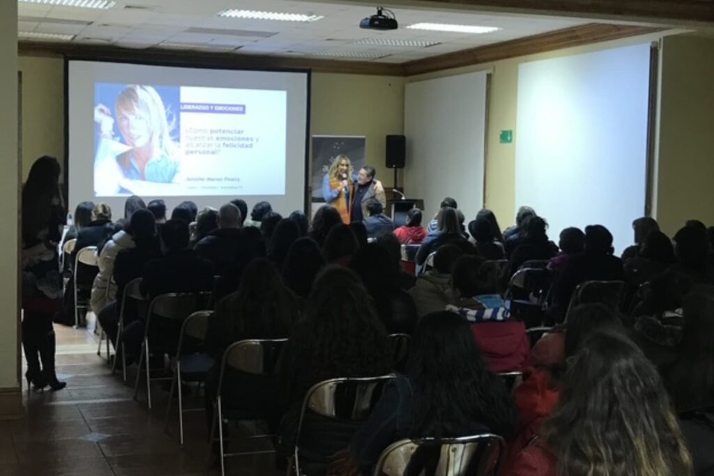Jennifer Warner realizando conferencia sobre liderazgo y emociones frente a un público atento en auditorio cerrado