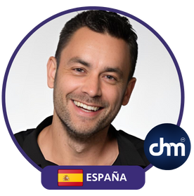 Fotografía de Achi Kushnir sonriendo, con camisa negra y fondo blanco, en un marco circular con la bandera de España y el logotipo de Charlas Motivacionales Latinoamérica.