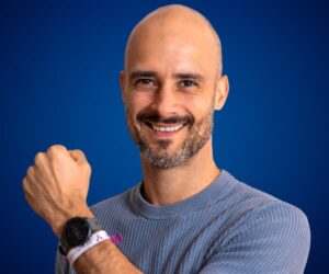 Felipe Corrales mostrando su reloj con actitud positiva y fondo azul