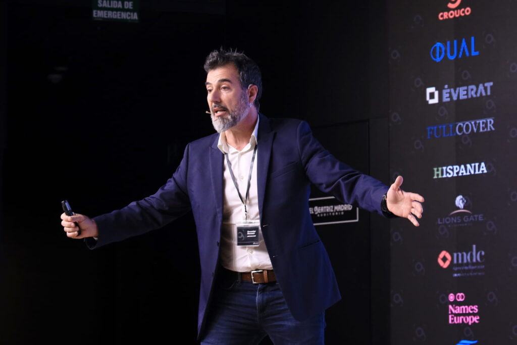Fotografía de Zacarías Romero ofreciendo una ponencia en el Auditorio Beatriz Madrid, gesticulando con entusiasmo frente a un fondo con logotipos de patrocinadores.