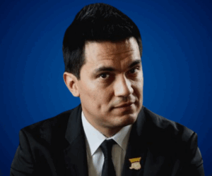 Fotografía de Germán Arciniegas con traje formal y fondo azul, mirando al frente con expresión seria y profesional.