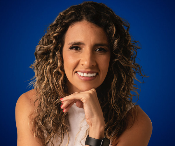 Fotografía de Karem Torres sonriendo frente a un fondo azul, con el rostro apoyado en su mano y cabello rizado suelto.