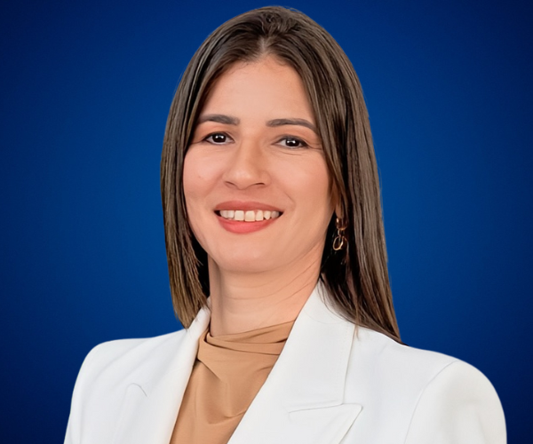 Retrato profesional de Mildred Ramírez con fondo azul, sonriendo con traje blanco.