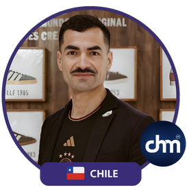 Fotografía de Octavio Díaz Matus, conferencista de Chile, posando con una expresión confiada frente a un fondo decorado con imágenes de calzado, vistiendo saco negro y camiseta deportiva.