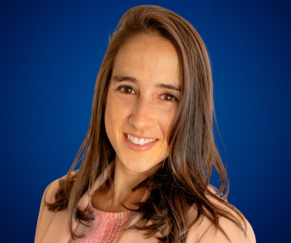 Sofia Spaggiari posando sonriente con fondo azul, vestida con chaqueta rosa claro