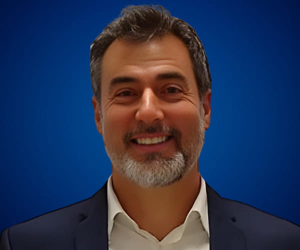 Fotografía de Zacarías Romero con fondo azul, luciendo una expresión cordial y profesional en un retrato de primer plano.