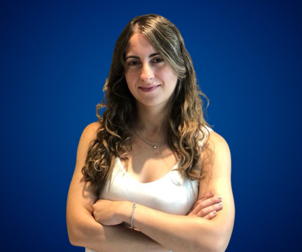 María Belén Sanmauro, con expresión confiada y los brazos cruzados, sobre un fondo azul liso que resalta su presencia profesional.