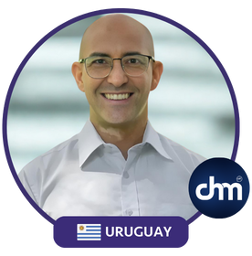 Fotografía de Carlos Bruzzone, conferencista uruguayo con saco a cuadros oscuros y camisa negra, posando con actitud segura sobre fondo blanco, enmarcado por diseño gráfico de evento.