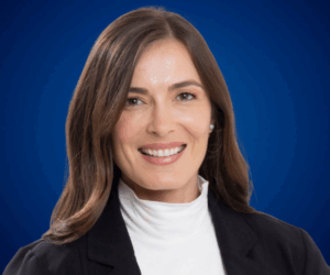 Fotografía de Catalina Serna, conferencista colombiana, con chaqueta negra y blusa blanca de cuello alto sobre fondo azul profesional.