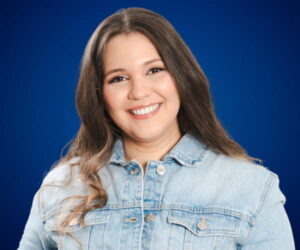 Fotografía de Danel Nouel con fondo azul, sonriendo y vistiendo una chaqueta de mezclilla en un retrato profesional.